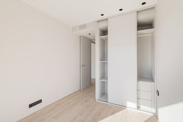 Empty clean bright bedroom with light wooden parquet and white wardrobe with sliding doors. A wardrobe is a useful and functional piece of furniture that saves space perfectly.