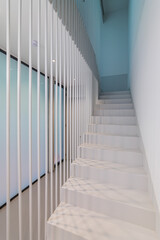 Beautiful white staircase to the second floor with soft blue lighting. Original design solution of the floor-to-ceiling fence made of metal white rods gives the effect of weightlessness.