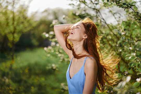 Woman with a beautiful smile with teeth and long hair in the spring sunset in nature in the park near the flowering trees happiness, natural beauty and hair health