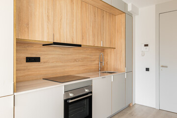 Contemporary minimal kitchen at empty refurbished apartment. Wooden furniture and modern appliances