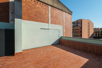 An empty spacious terrace on the second floor of a large house with a brick red floor for relaxing on warm summer evenings in the sun of the passing day. Sunlight illuminates the site.