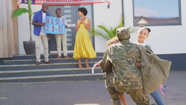 Children run to hug Dad as multi-generation family welcome army father home on leave with banner - shot in slow motion