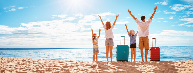 Mother and father with their children standing on the beach with suitcases. - 560671473