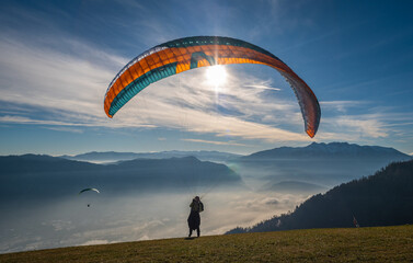 Man on a grassy slope prepare the glider for paragliding from Vetriolo Terme, Trento province -...