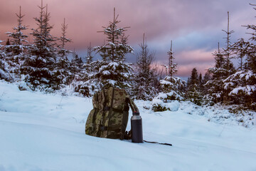 Obraz premium A backpack in military coloring and a thermos on a winter landscape in the forest.
