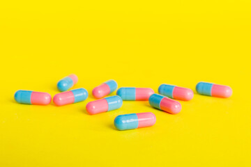 Heap of pink and blue pills on colored background. Tablets scattered on a table. Pile of red soft gelatin capsule. Vitamins and dietary supplements concept