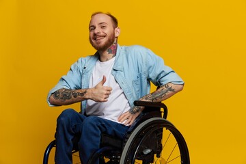 A man in a wheelchair smile and happiness, thumb up, with tattoos on his hands sits on a yellow...