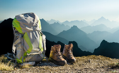 Hiking equipment with blue moutain silhouettes. Backpack and boots on top of mountain. Tyrol, Austria. - 560674664