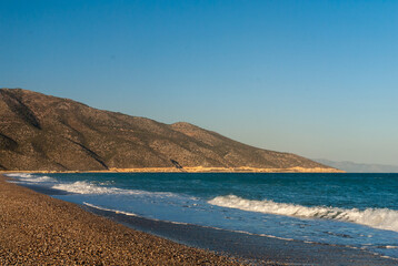View of Turkish Mediterranean coast. Automobile road along mountains on coast. Emerald water washes pebbly shore. Blurred background. Selective focus. Wild Mediterranean beach. Turkey. Fethiye.