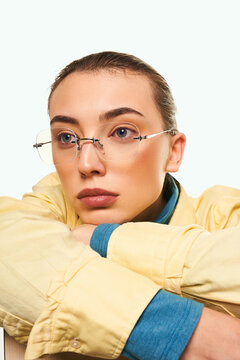 Cropped close-up shot of a woman wearing fashion rimless glasses with clear lenses and with thin temples. A woman in a yellow shirt with glasses without frames is on a light background. Front view.