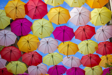 Fototapeta na wymiar Background of lots of colorful brightly colored umbrellas in a blue sky view from below. Festive festival decorations of the city streets. Travel and leisure concept. Multicolor umbrellas hanging.