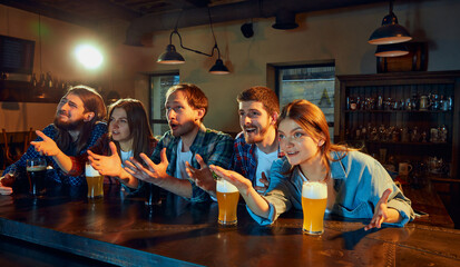 Friends meeting. Young people, men and women watching match at pub. Fans emotionally cheering up...