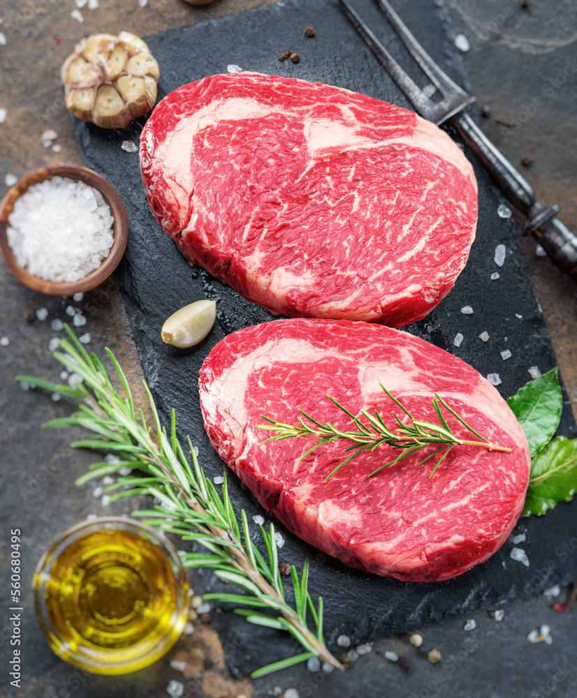 Wall mural raw ribeye steaks with rosemary and other seasoning on gray tray. top view.