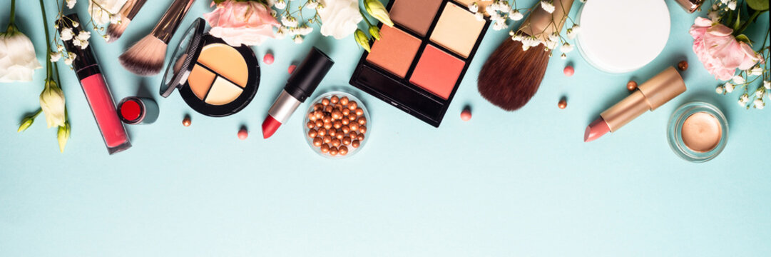 Make up professional cosmetics on blue background. Cream, powder, shadow, brushes with green leaves and flowers. Long banner format.