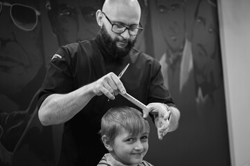 Happy cute fair-haired preschool boy getting a haircut. Children's hairdresser with scissors and...