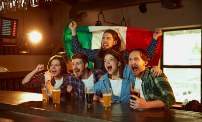Group of young people, men and women watching match at pub. Fans emotionally cheering up favourite sport team. Italy