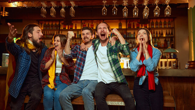 Group of young people, friends, emotionally watching match at pub. Fans cheering up favourite sport team. Winning game. Success