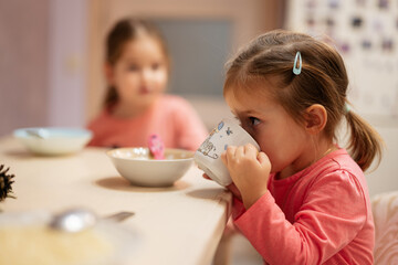 Two sisters have dinner together in the kitchen, baby girl drinks from a cup.