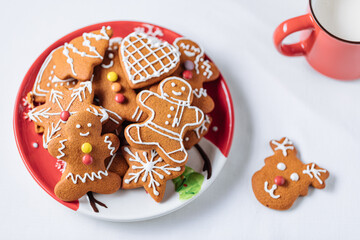 Gingerbread cookies in shape of ginger man placed on red plate. White background. Traditional Christmas dessert decorated. Playful and happy.