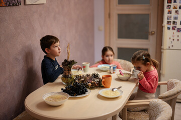 Three kids have dinner together in the kitchen.