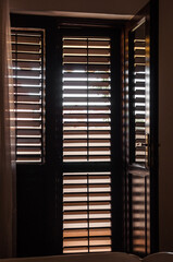 A room with an opened door to the balcony and closed wooden blinds.