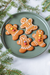 Gingerbread cookies in shape of ginger man placed on green plate with pine tree as decoration. Traditional Christmas dessert decorated. Playful and happy.