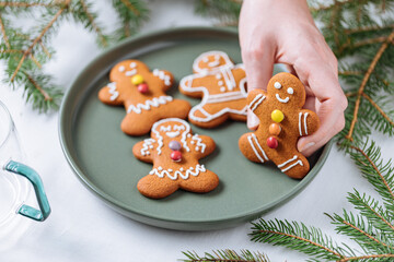 Gingerbread cookies in shape of ginger man placed on green plate with pine tree as decoration. Traditional Christmas dessert decorated. Playful and happy.