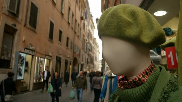 Fashionable dummy with winter clothes outdoor in a shopping street in the historical centre of Rome, Italy. People and tourists on the blurred background. Selective focus.