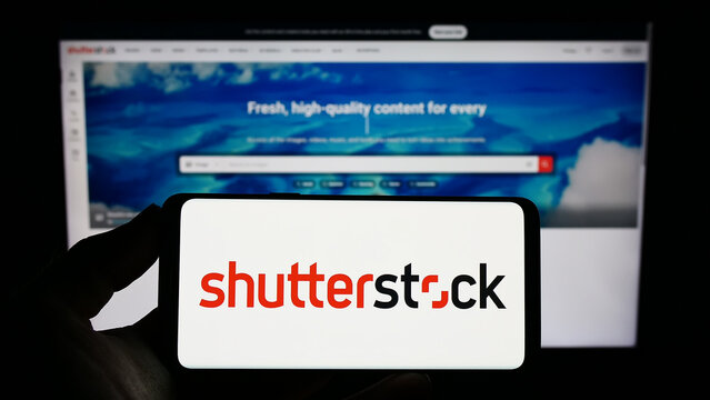 Stuttgart, Germany - 01-08-2023: Person holding smartphone with logo of US stock photography company Shutterstock Inc. on screen in front of website. Focus on phone display.
