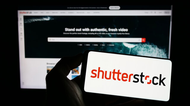 Stuttgart, Germany - 01-08-2023: Person holding mobile phone with logo of US stock photography company Shutterstock Inc. on screen in front of web page. Focus on phone display.