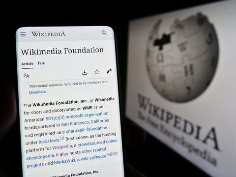 Stuttgart, Germany - 01-08-2023: Person holding smartphone with web pag eof online encyclopedia Wikipedia on screen in front of logo. Focus on center of phone display.