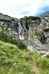 Waterfall with rocks, green grass and blue sky. Waterfall in High Tatra mountains. Beautiful Slovak nature. Hiking and nature concept. © stefanbalaz