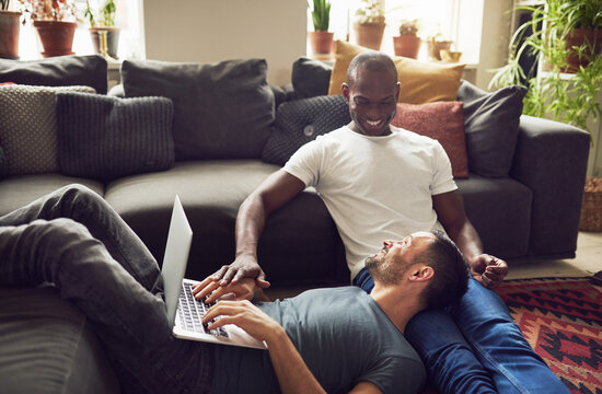 Two multiethnic gay lovers on floor with laptop