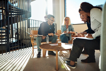 Diverse businesspeople laughing while discussing paperwork during a meeting