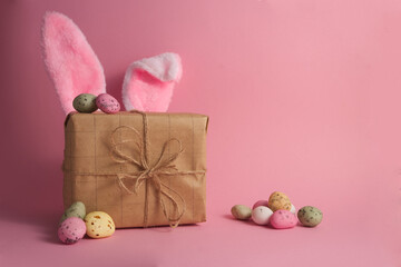 Gift box with cute bunny ears and easter eggs on pink background copy space