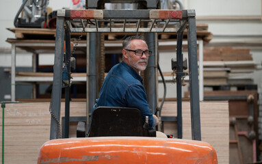 Fototapeta na wymiar Male factory manager working in warehouse driving forklift truck. Portrait of forklift driver employee transporting merchandise in storehouse delivering to shelf. Industrial worker in industry vehicle