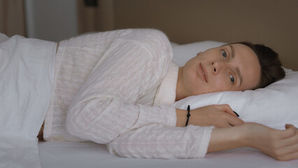 Sleepy woman waking up, turning on the pillow, smiling and stretching on the bed