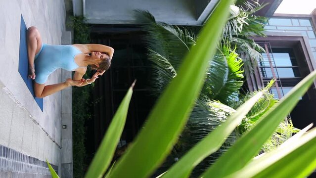 A woman practices yoga near palm trees, does stretching, tropics of Asia