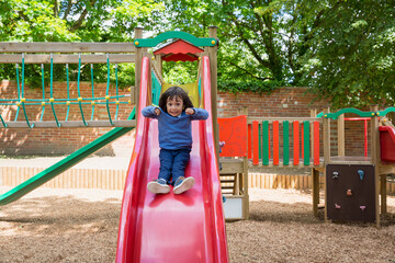 Handsome active little boy having fun while playing and sliding on the outdoor playground. Kids...