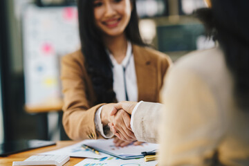 Two young Asian businesswomen shaking hands in a successful business in finance co-investment banking agreement concept.