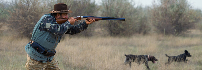 Hunter man in camouflage with a gun during the hunt in search of wild birds or game.