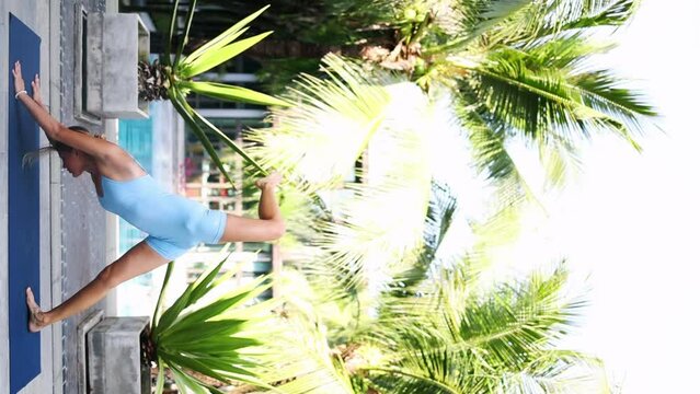 A woman practices yoga near palm trees, does stretching, tropics of Asia