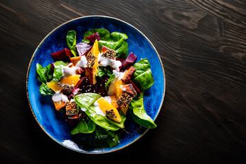 vegetarian salad with beets, spinach, orange, tofu in plate on wooden table background