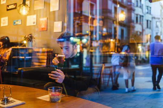 Pensive man enjoying beverage in bar with smartphone