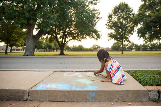Young girl playing with chalk on neighborhood sidewalk