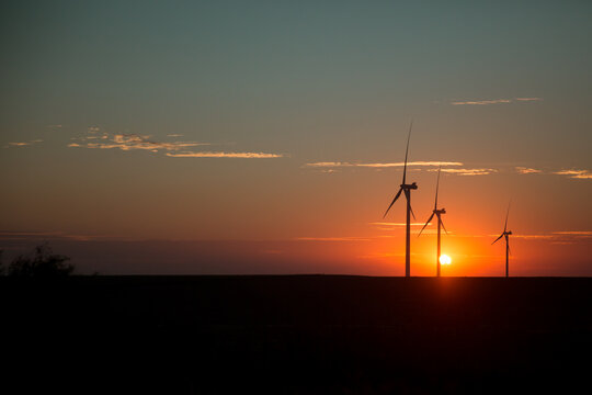 Three wind turbines against sunset in field