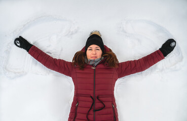 Fototapeta na wymiar Top view of woman in red winter coat making snow angel on winter day.