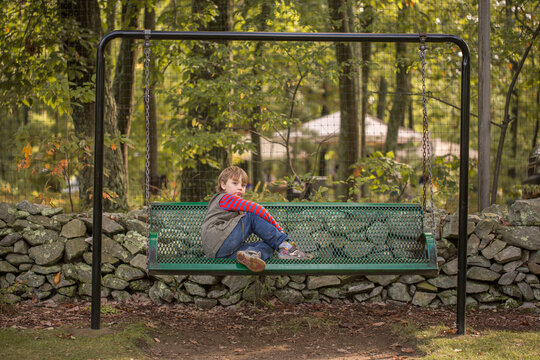 Boy sitting alone on green bench porch swing in front of stone wall