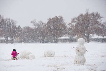 Girl in pink rainbow snowsuit building snowman