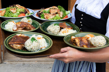 The waiter holds national Bavarian dishes, bread dumplings, meat and cabbage on a tray.